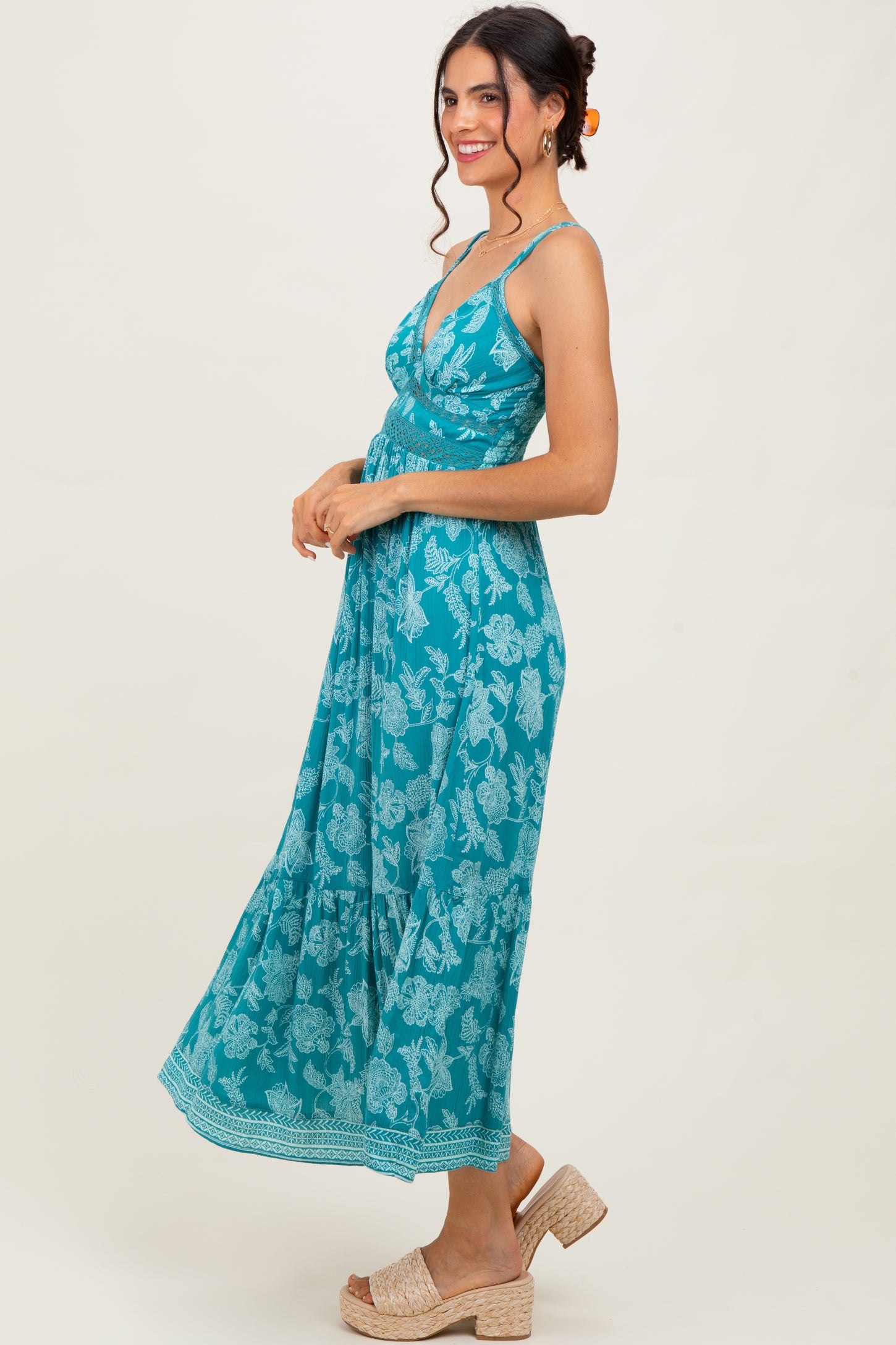 woman wearing a turquoise maxi dress with floral print and a tiered skirt, styled with woven sandals