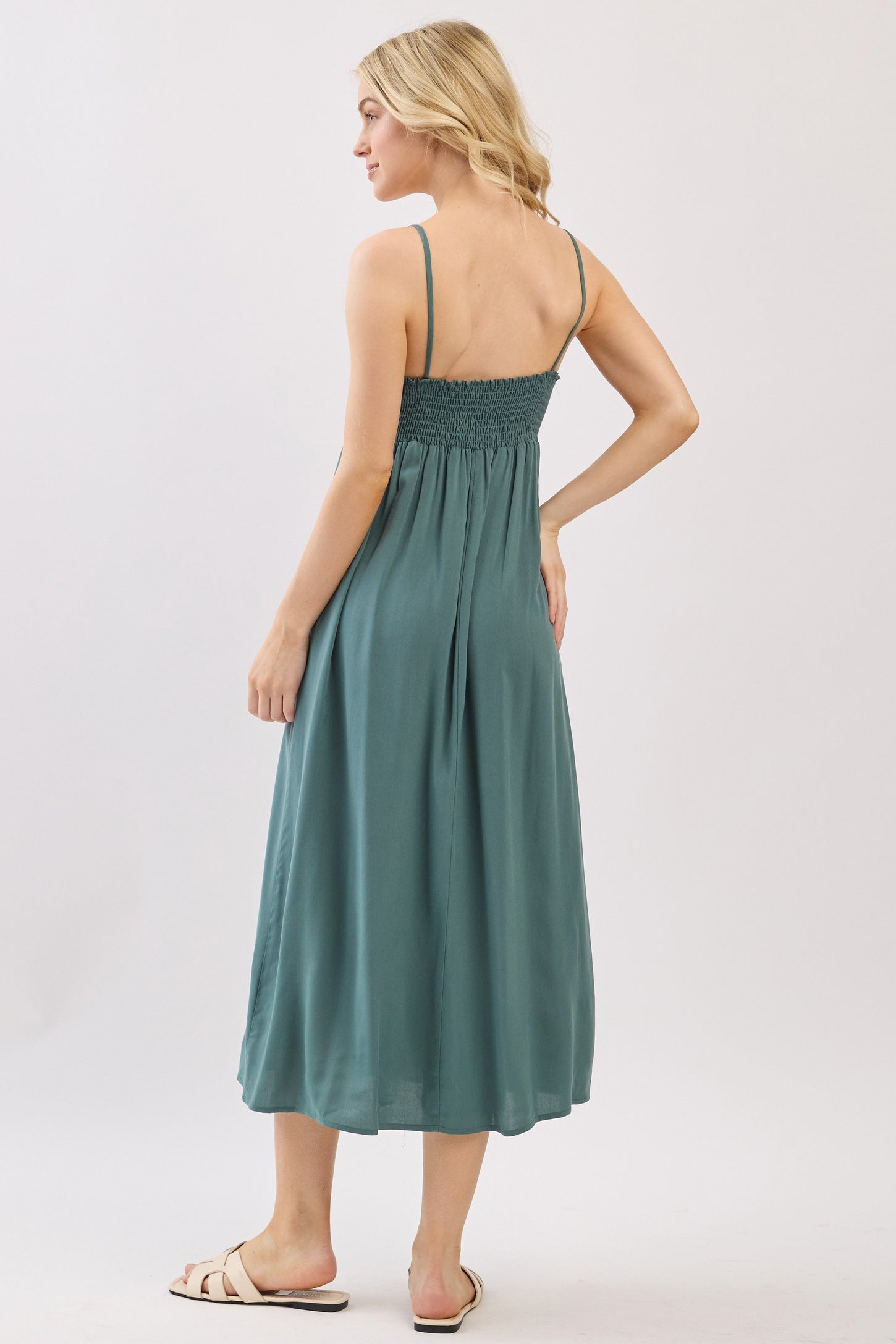 woman wearing a teal sleeveless midi dress with a smocked back and flowing silhouette