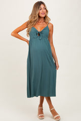 woman wearing a dark teal maternity dress with a front knot and a visible baby bump