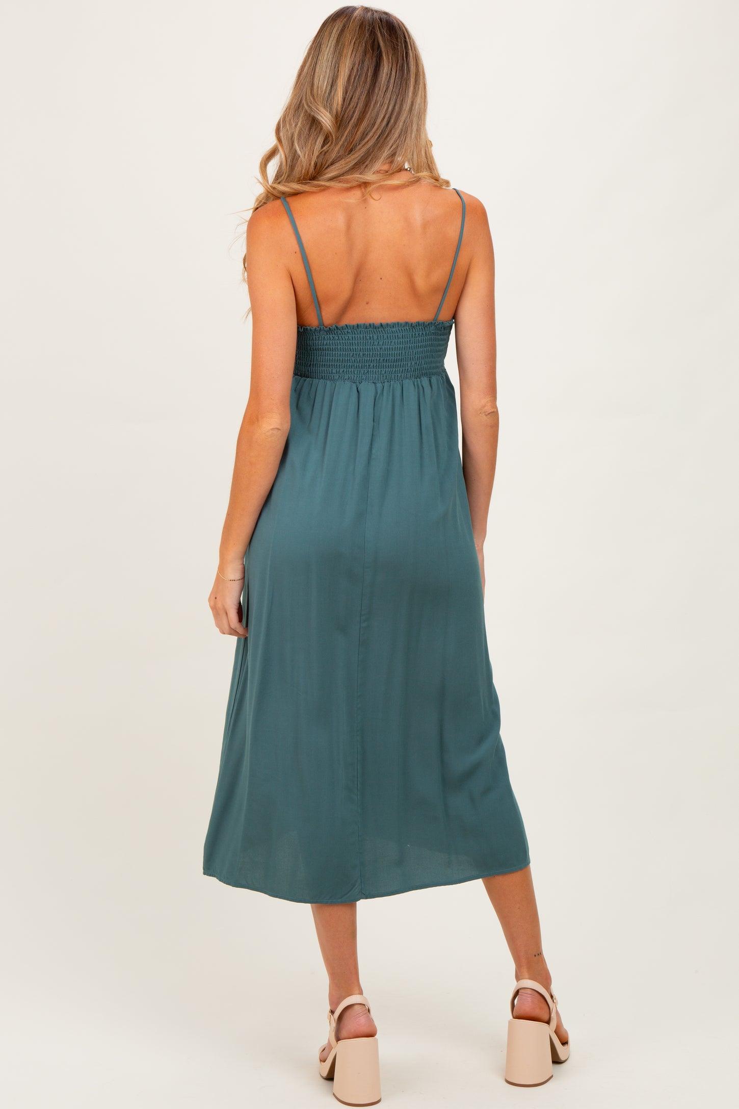 woman wearing a teal maternity dress with a smocked back and adjustable spaghetti straps, shown from the back
