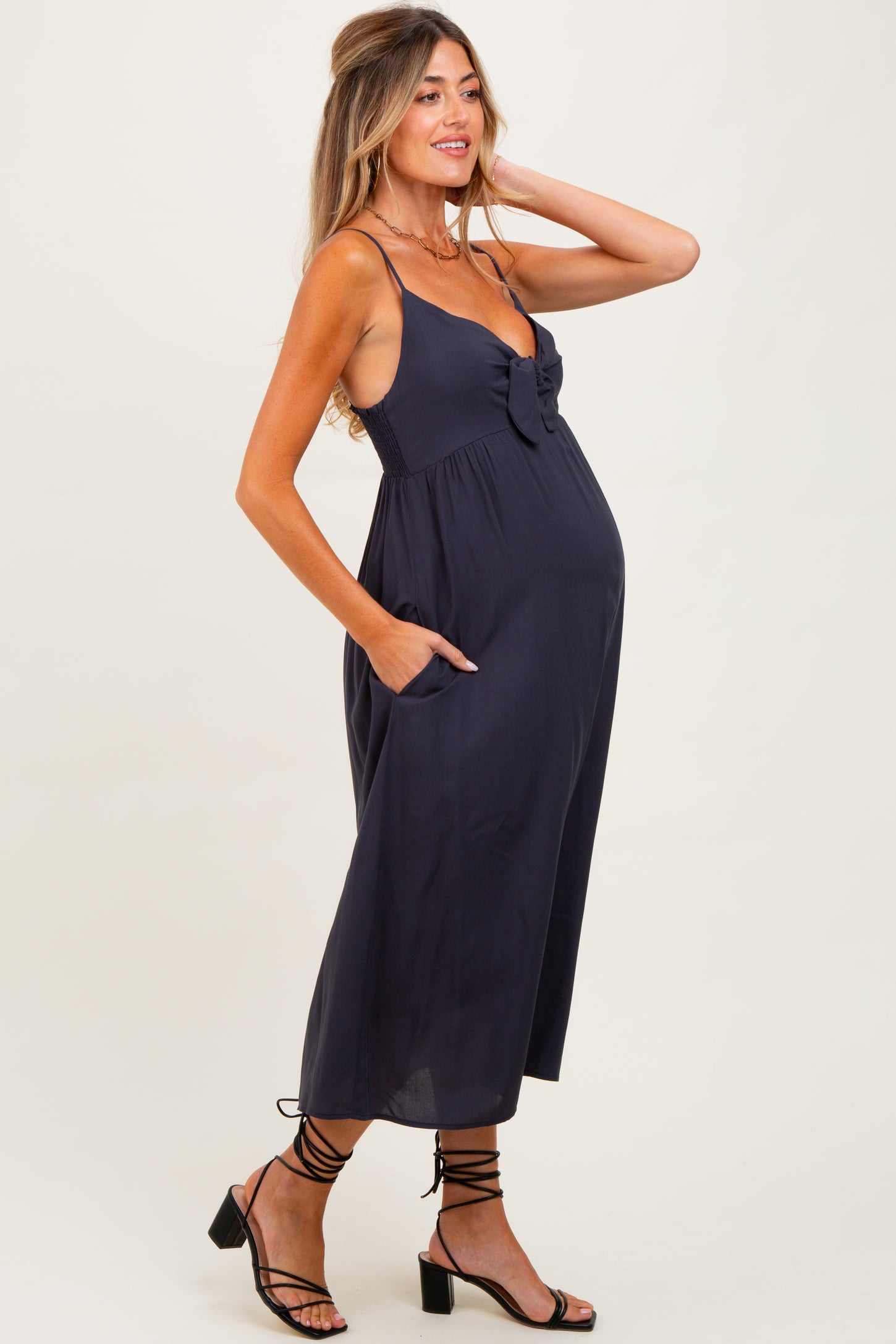 woman wearing a navy blue maternity dress with a bow detail and pockets, showing a visible baby bump