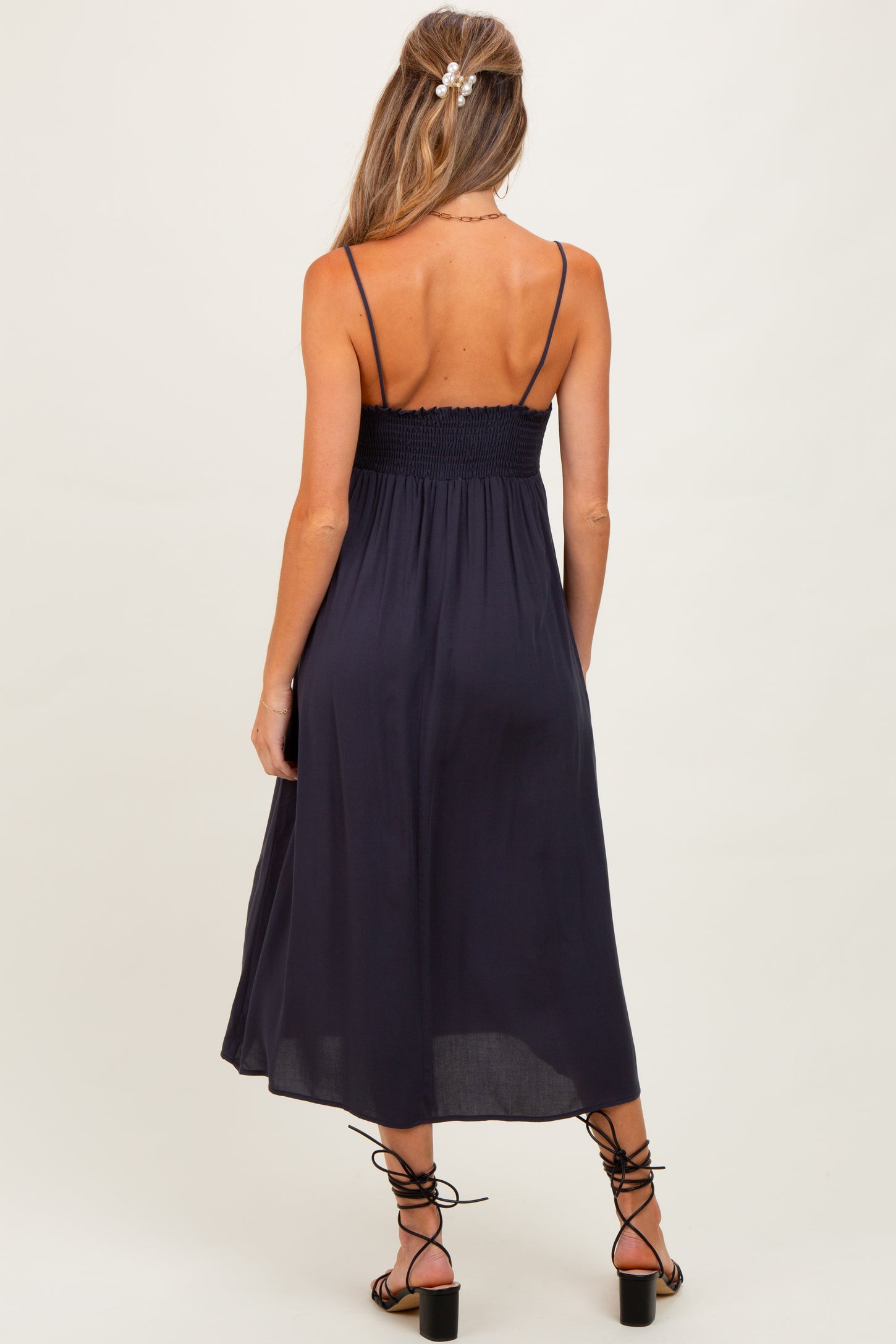 woman wearing a navy blue maternity dress with a smocked bodice and spaghetti straps, showing her back