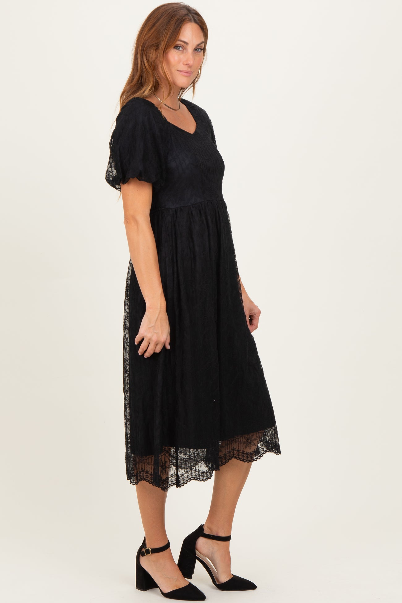 woman wearing a black midi dress with a textured bodice, puff sleeves, and lace detailing at the hem
