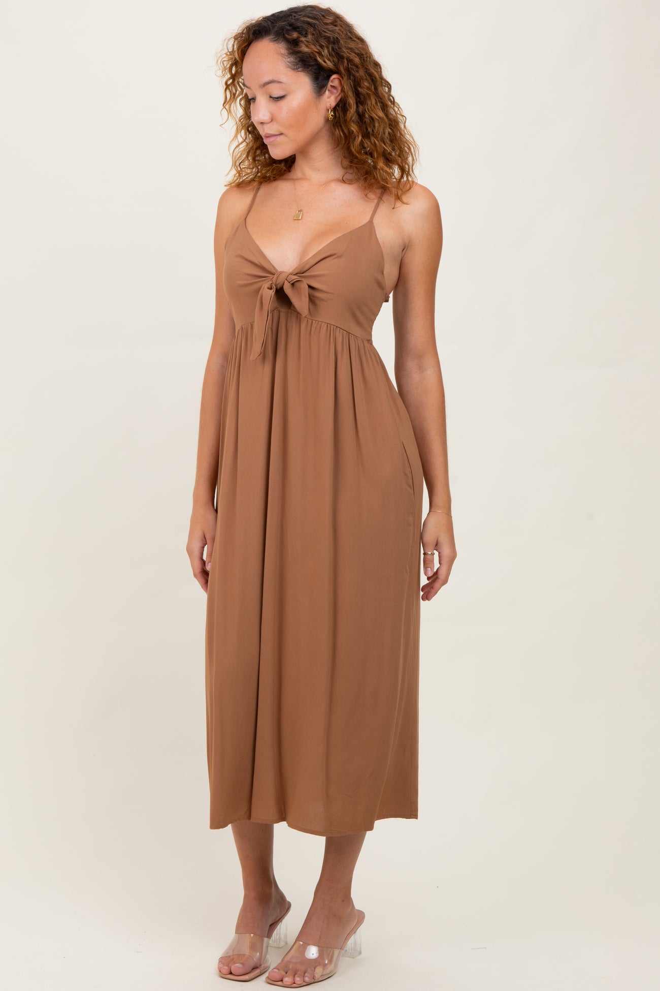 woman wearing a brown spaghetti strap midi dress with a front tie detail and a flowing silhouette