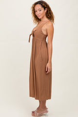woman wearing a brown sleeveless maxi dress with a tie detail at the bust and side pockets