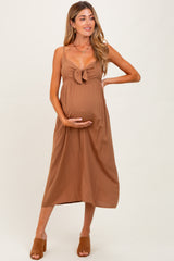 woman wearing a brown maternity dress with a bow detail, holding her baby bump and smiling