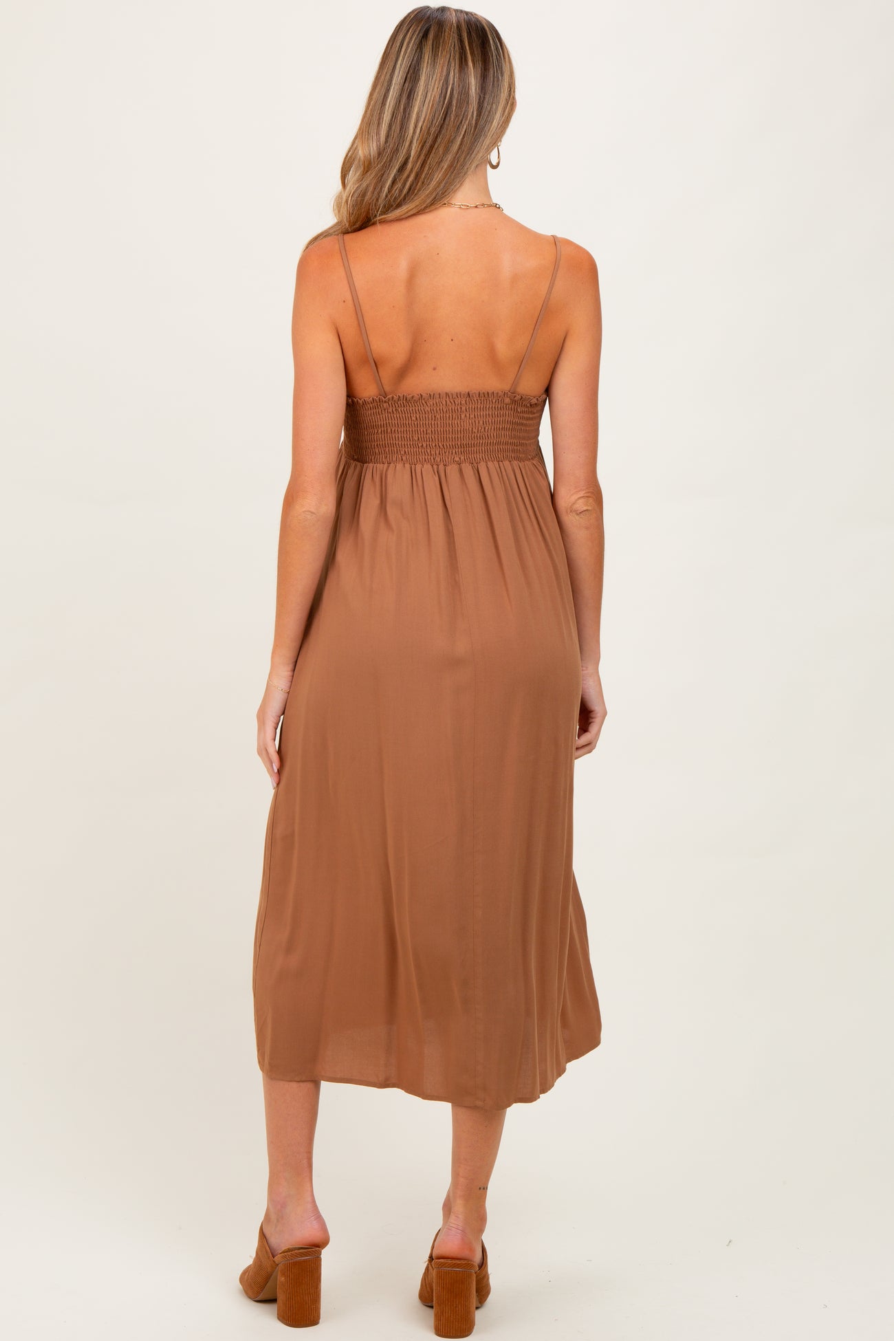 woman wearing a brown maternity dress with a smocked back and spaghetti straps, showing off a baby bump