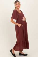 woman wearing a burgundy maternity dress with short sleeves, a square neckline, and a tiered skirt, showing her baby bump