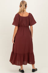 woman wearing a burgundy maternity maxi dress with short puff sleeves and a tiered hem, showcasing a baby bump