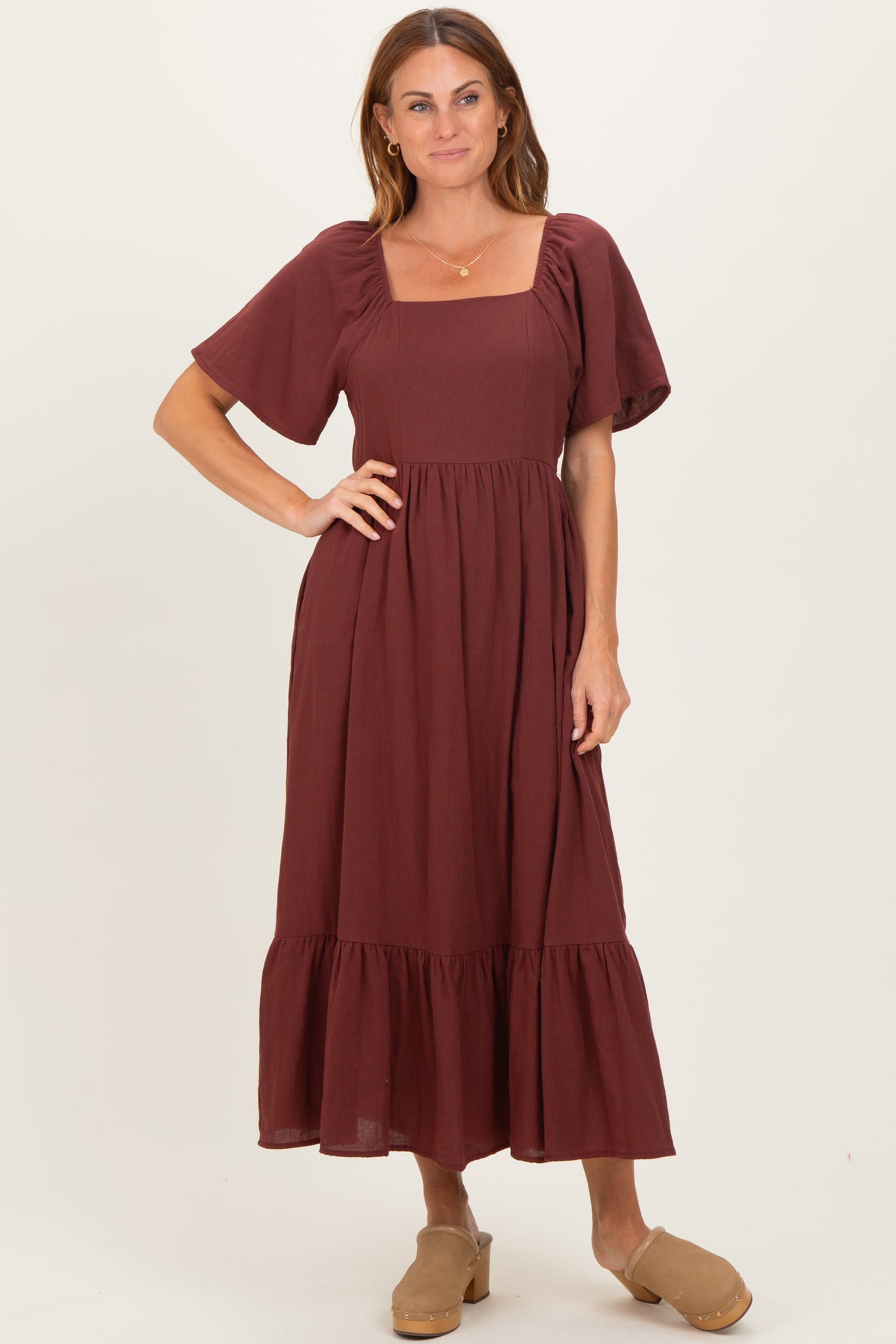 woman wearing a burgundy maxi dress with a square neckline and puff sleeves, styled with tan clogs