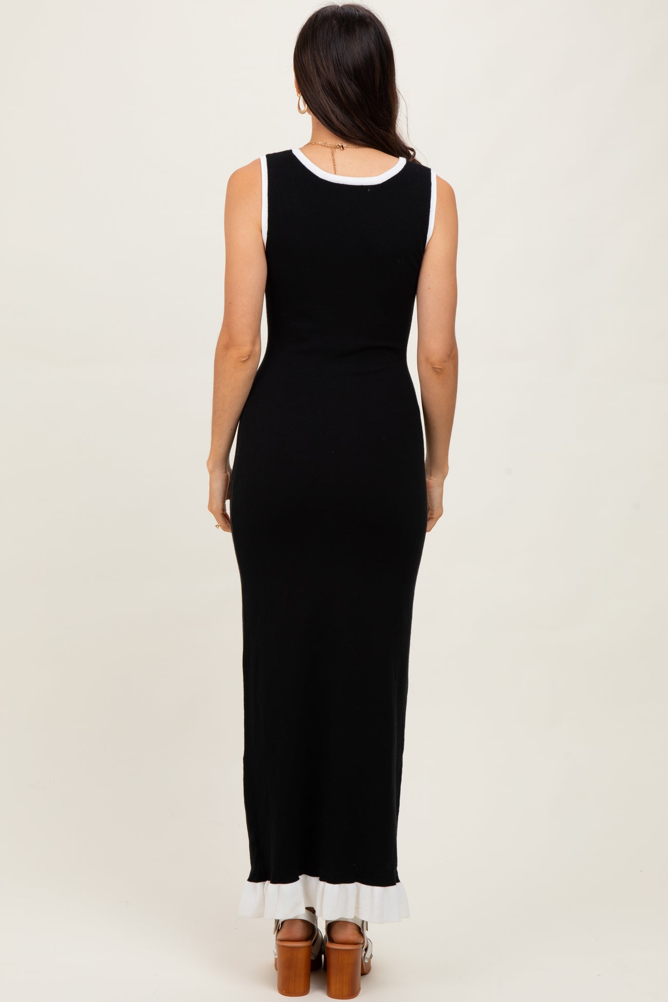 woman wearing a sleeveless black maxi dress with a white trim at the hem and a fitted silhouette