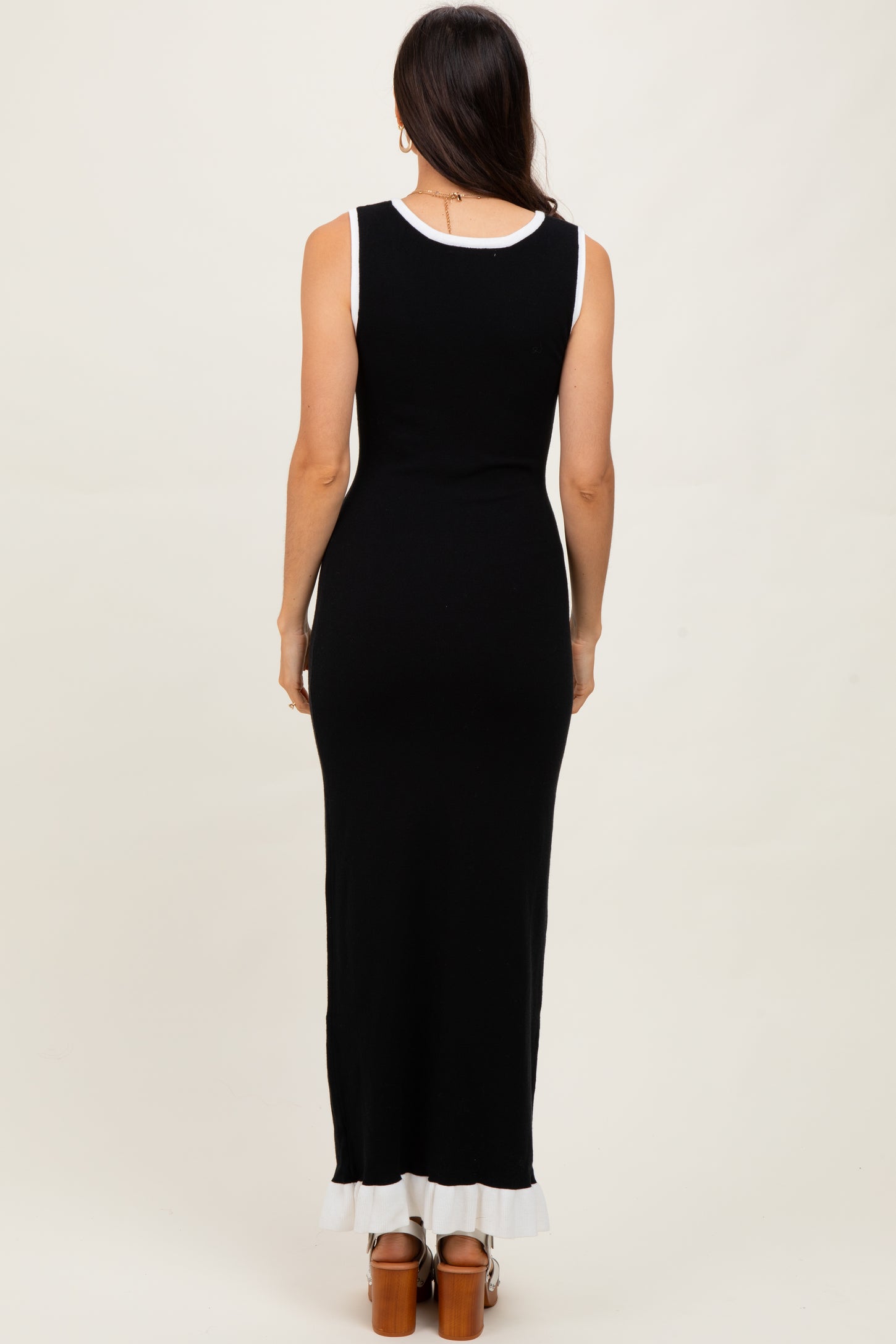 woman wearing a sleeveless black maxi dress with a white trim at the hem and a fitted silhouette