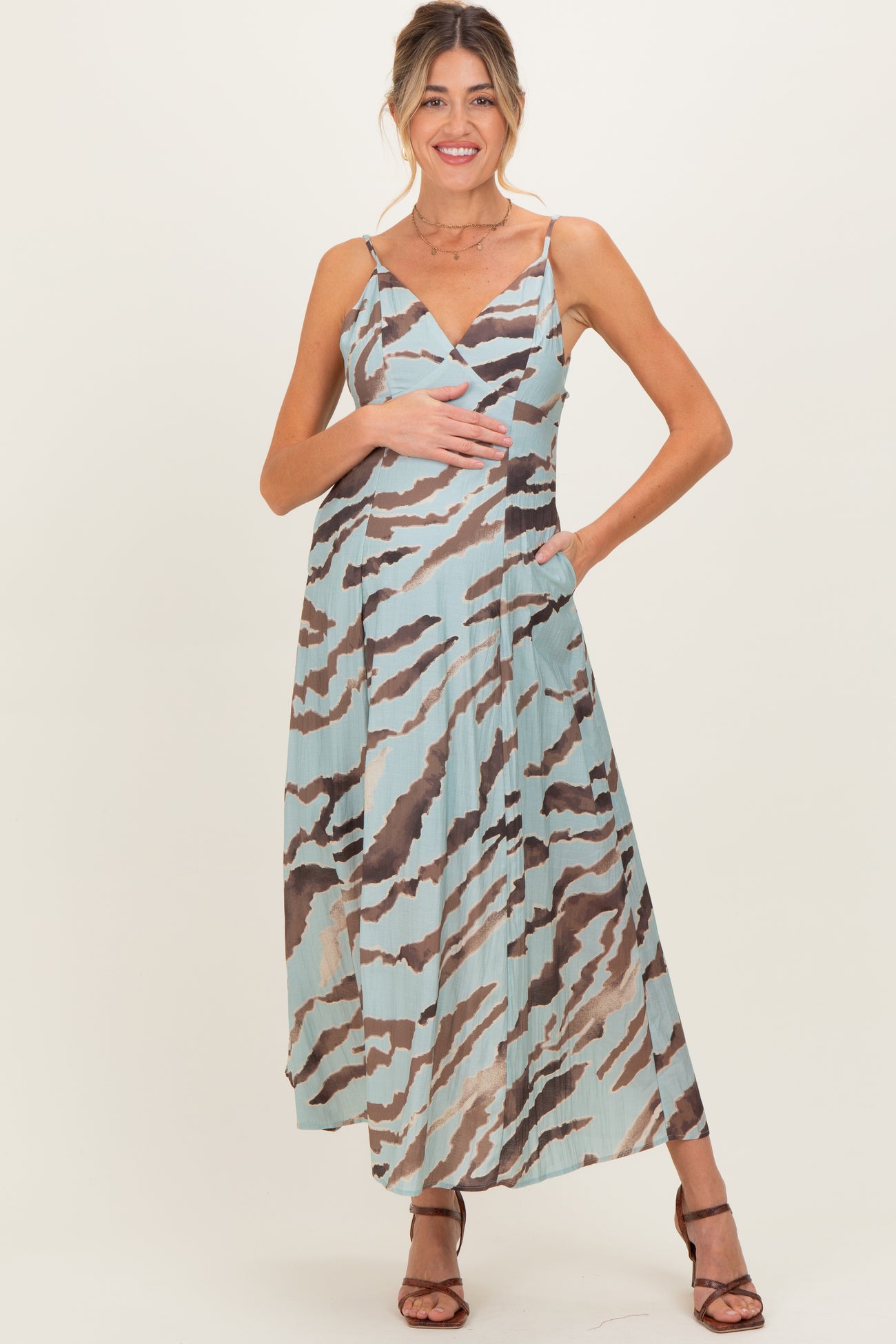 woman wearing a patterned maxi maternity dress in blue and brown, holding her baby bump with a smile