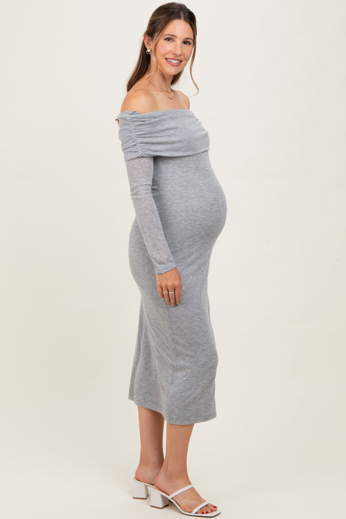 woman wearing a gray off-the-shoulder maternity dress, showcasing her baby bump, standing against a neutral background