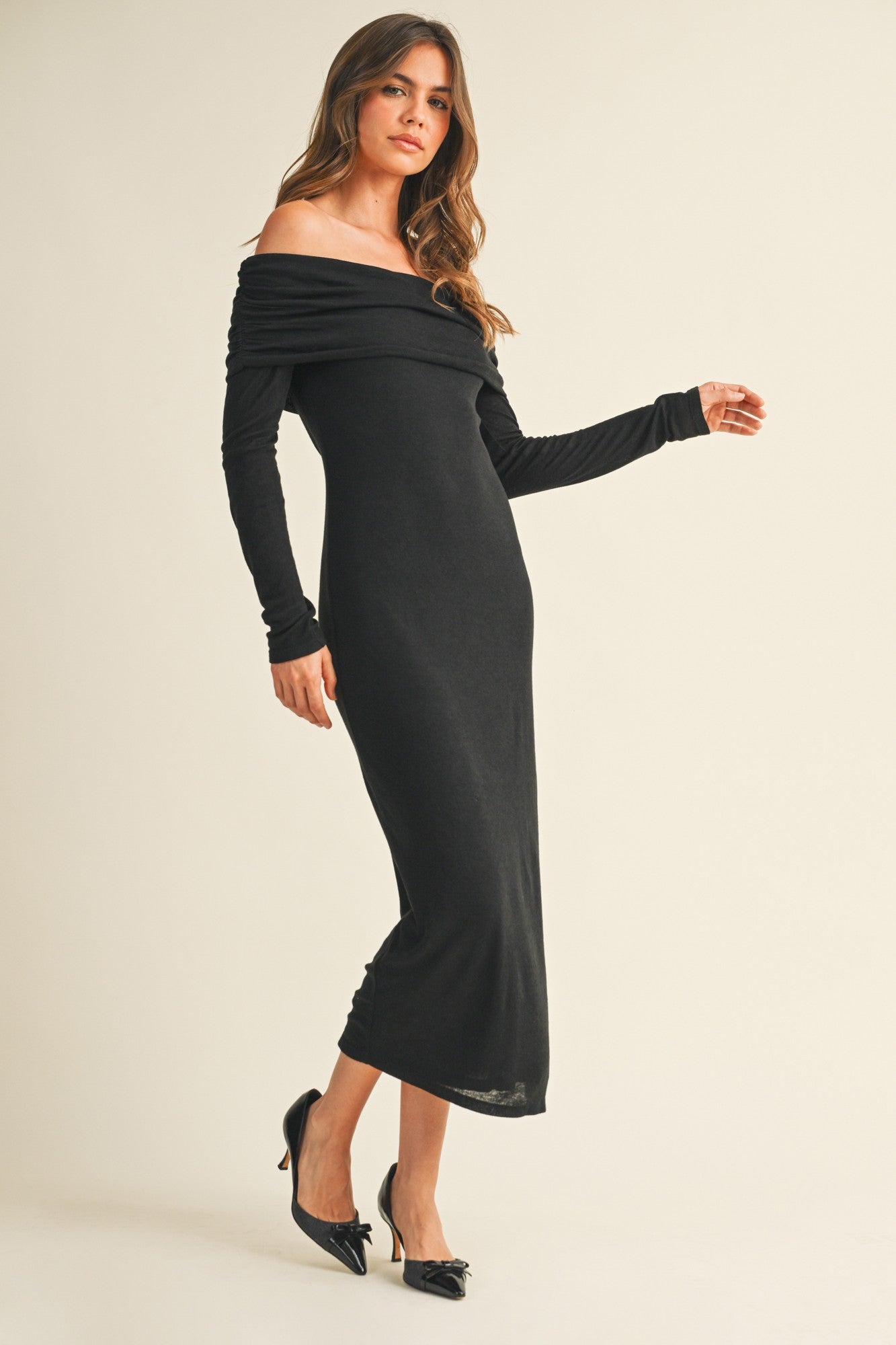 woman wearing a black off-the-shoulder long sleeve dress, styled with a fitted silhouette and high slit, paired with black heels