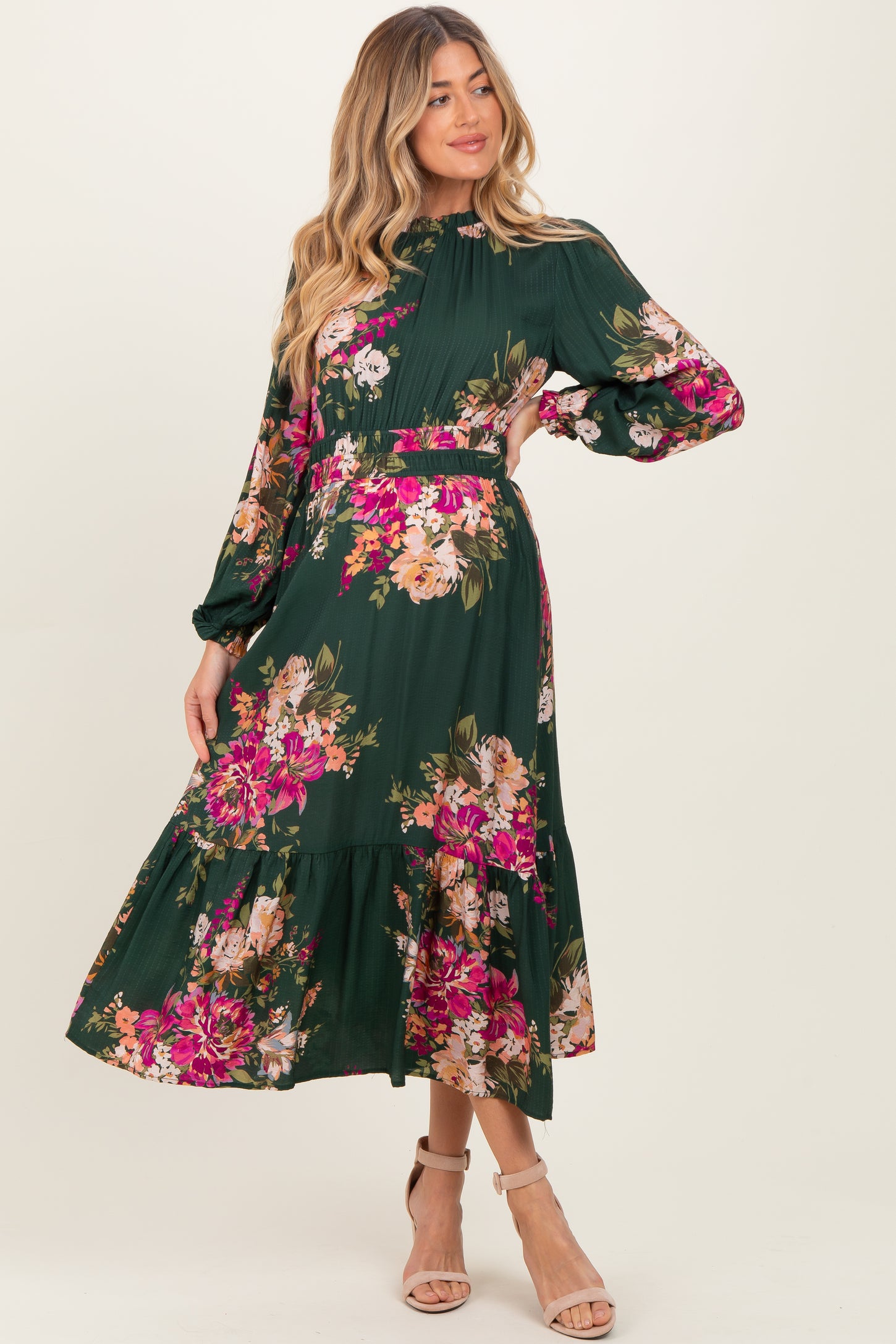 woman wearing a green floral maternity dress with long sleeves and a tiered skirt, showcasing her baby bump