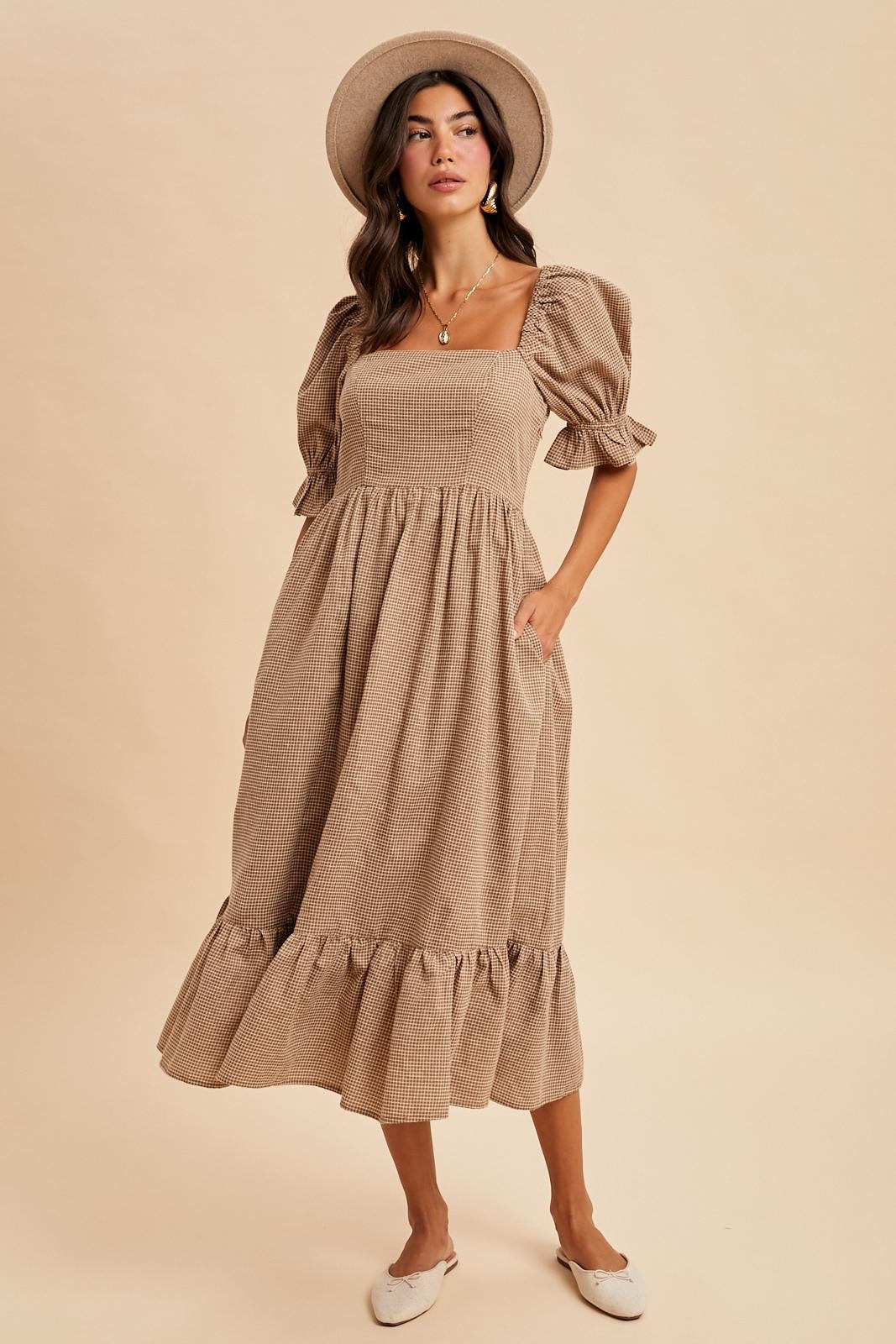 woman wearing a taupe puff sleeve midi dress with a square neckline and ruffled hem, styled with a hat and flats