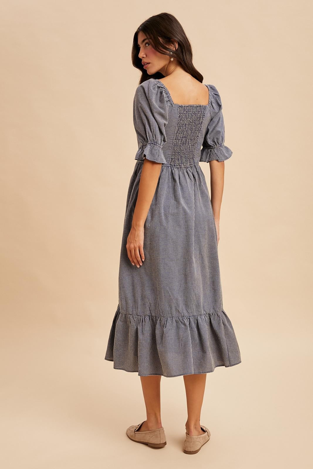 woman wearing a navy blue gingham midi dress with puff sleeves and a ruffled hem, facing away from the camera