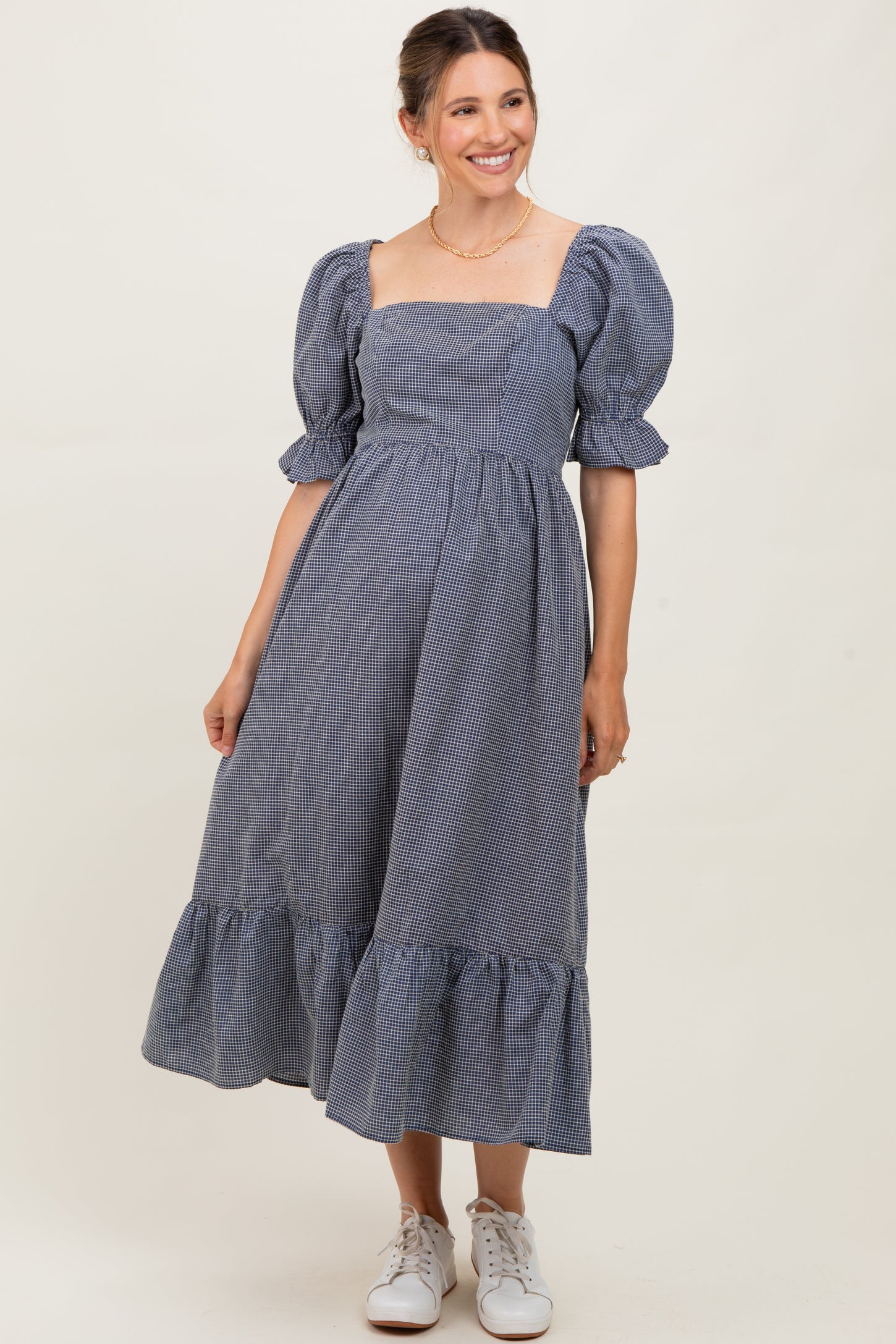 woman wearing a navy and white checkered maternity dress with puff sleeves and a tiered skirt, smiling at the camera