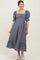 woman wearing a navy and white checkered maternity dress with puff sleeves and a tiered skirt, smiling at the camera