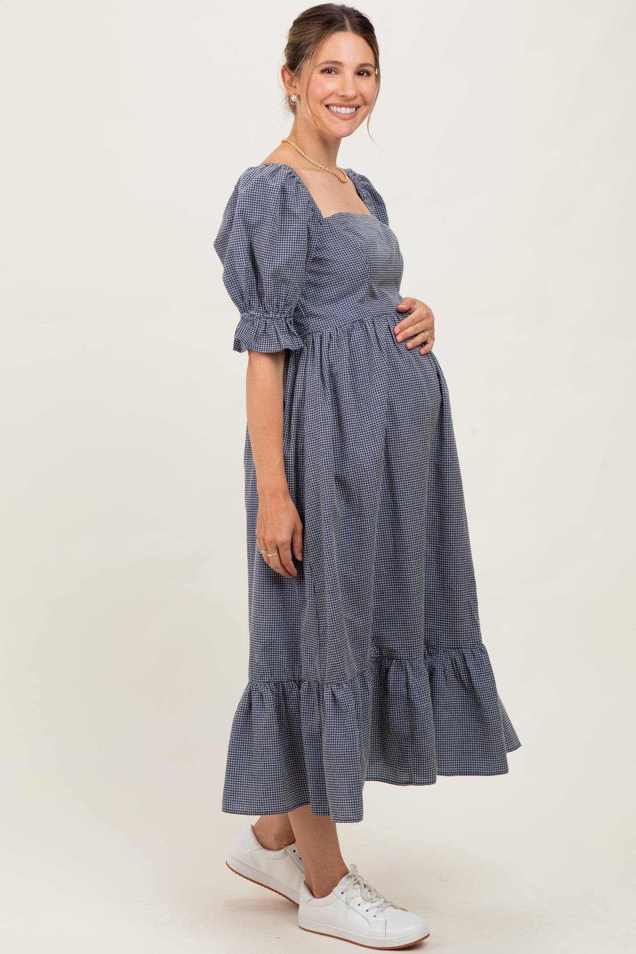 woman wearing a navy and white gingham maternity dress with puff sleeves and a ruffled hem, holding her baby bump