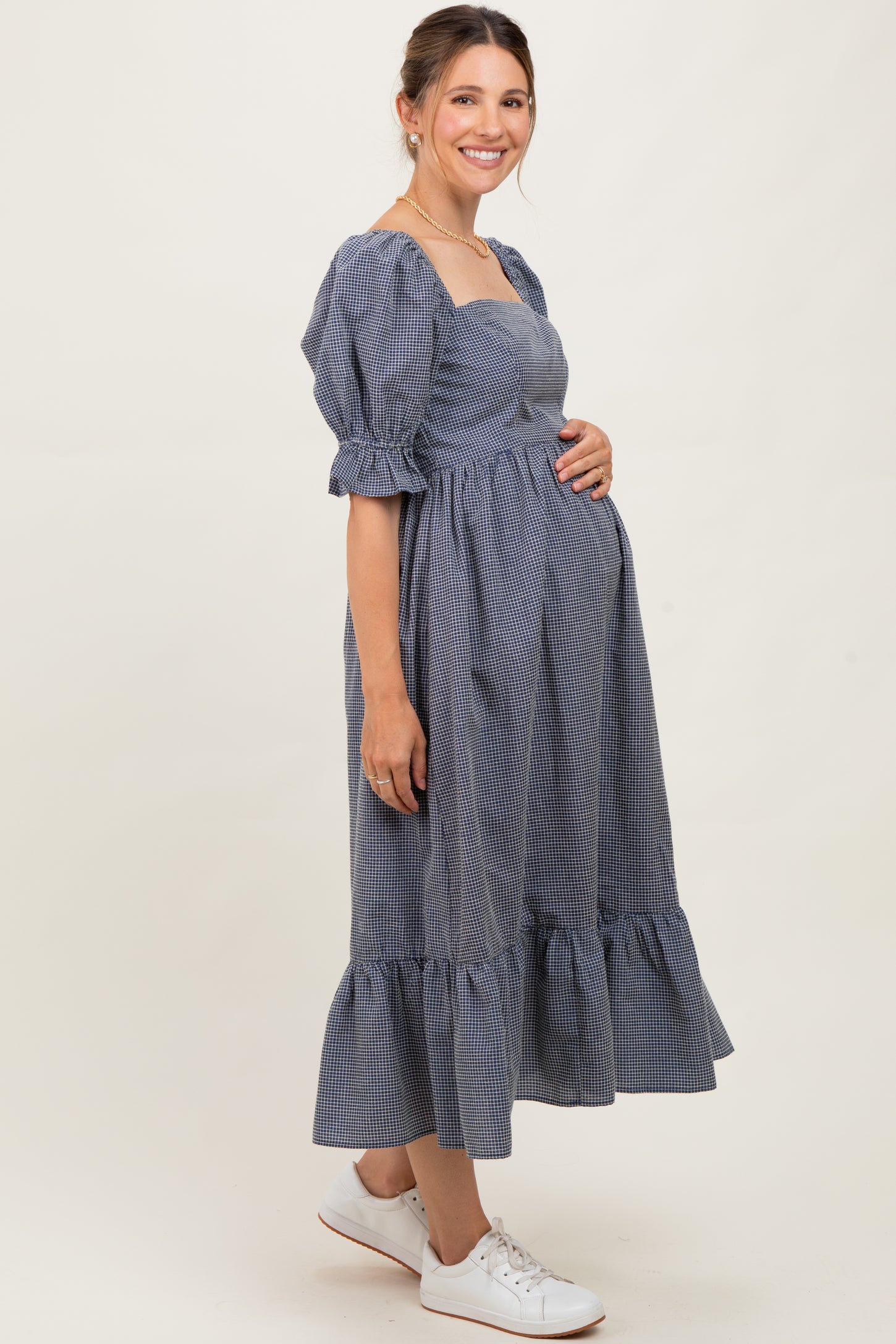 woman wearing a navy and white gingham maternity dress with puff sleeves and a ruffled hem, holding her baby bump
