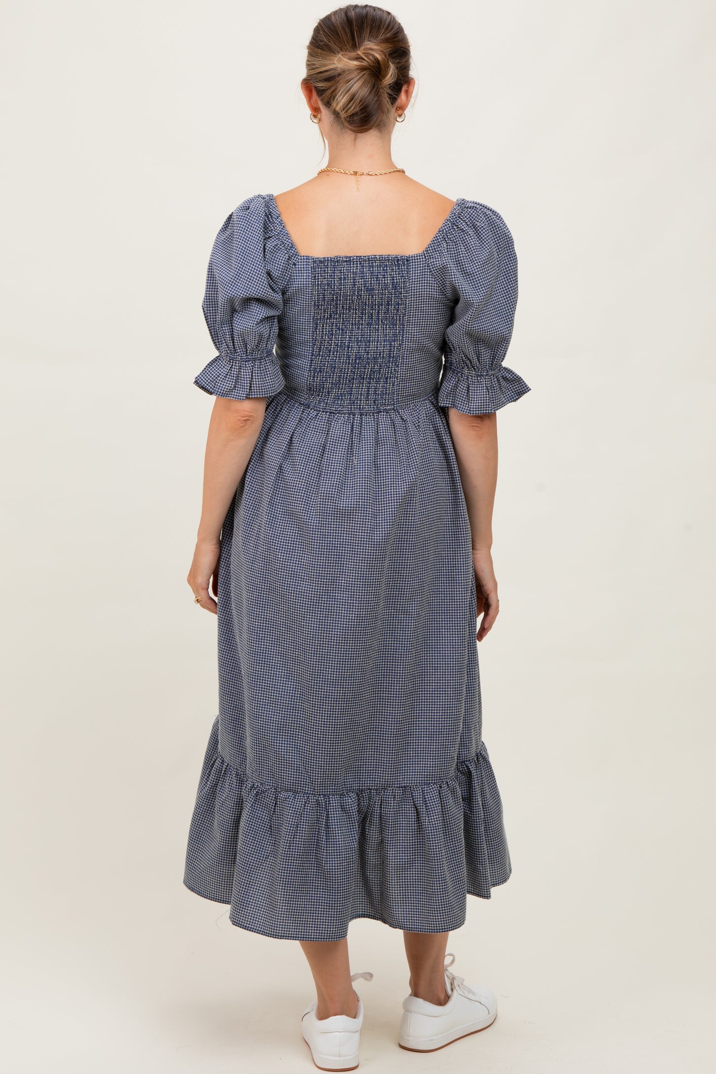 woman wearing a navy and white checkered maternity dress with puff sleeves and a ruffled hem, showing a baby bump