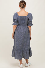 woman wearing a navy and white checkered maternity dress with puff sleeves and a ruffled hem, showing a baby bump