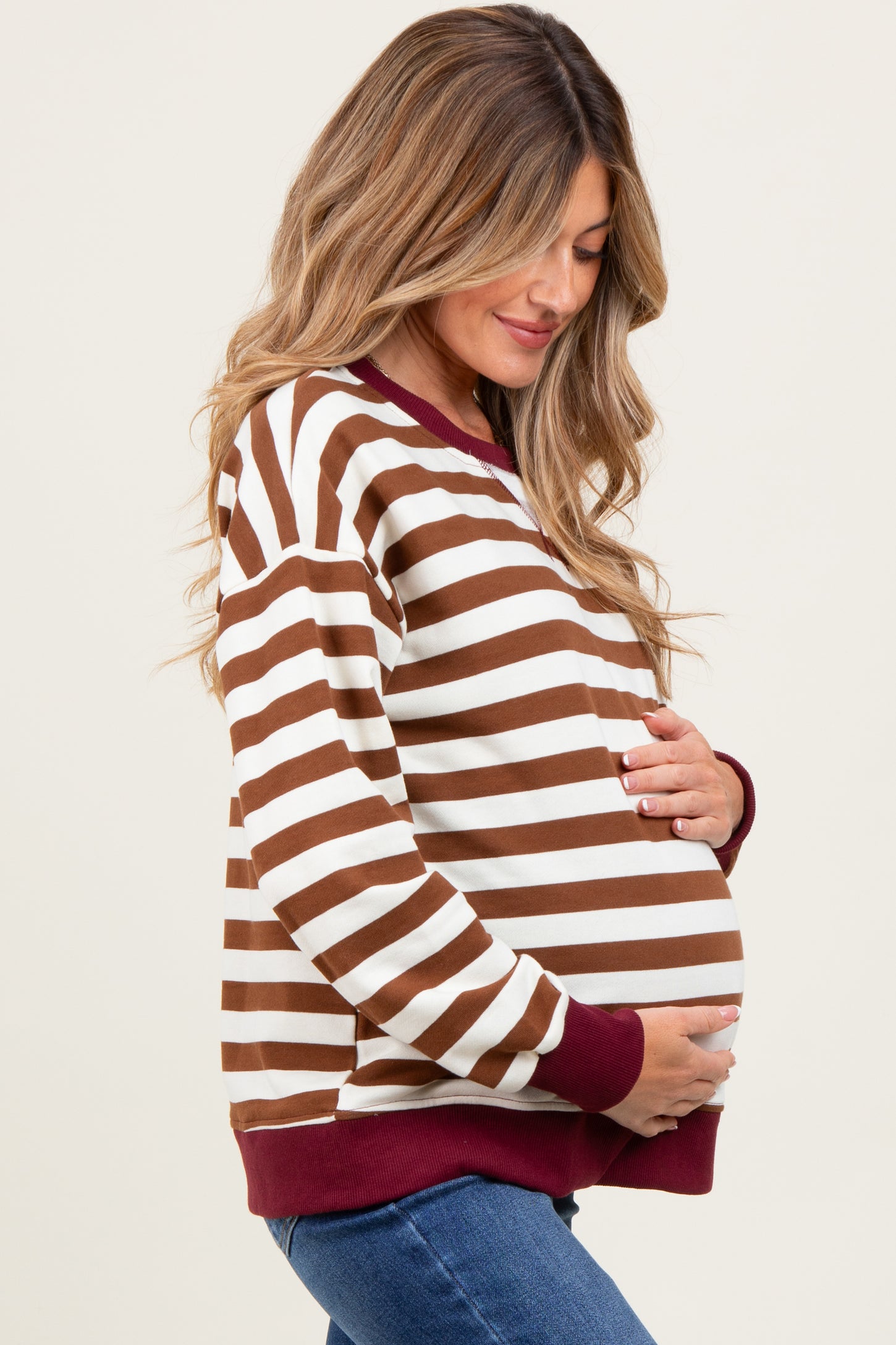 woman wearing a brown and white striped maternity sweatshirt with maroon accents and holding her baby bump
