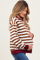 woman wearing a brown and white striped maternity sweatshirt with maroon accents and holding her baby bump