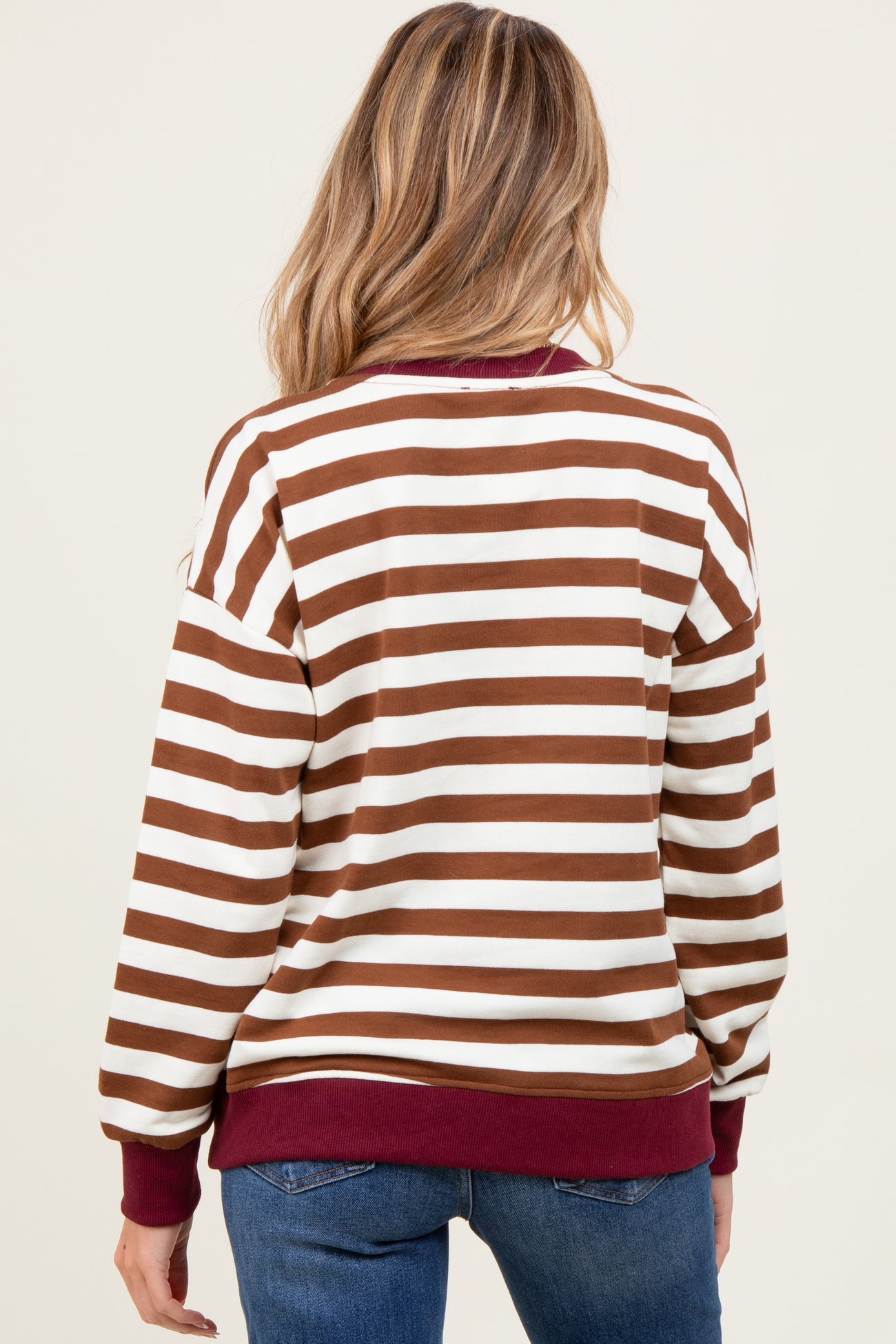woman wearing a brown and white striped maternity sweatshirt with a maroon waistband and cuffs, viewed from the back