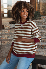 woman wearing a brown and cream striped maternity sweatshirt with a red neckline, gently cradling her baby bump