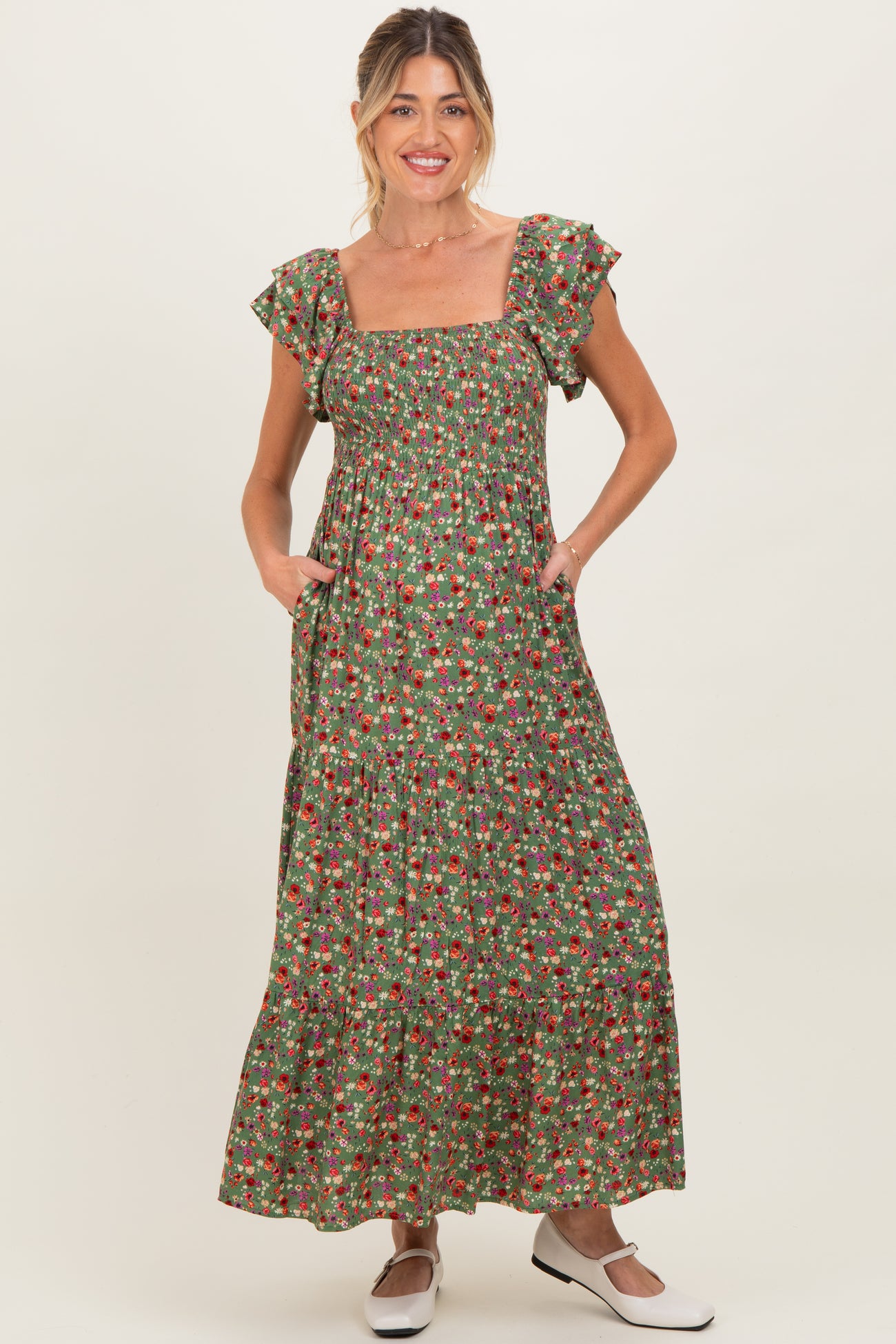 woman wearing a floral print green maternity maxi dress with ruffle sleeves and pockets, standing against a neutral background