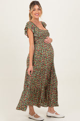 woman wearing a green floral maternity maxi dress and cradling her baby bump