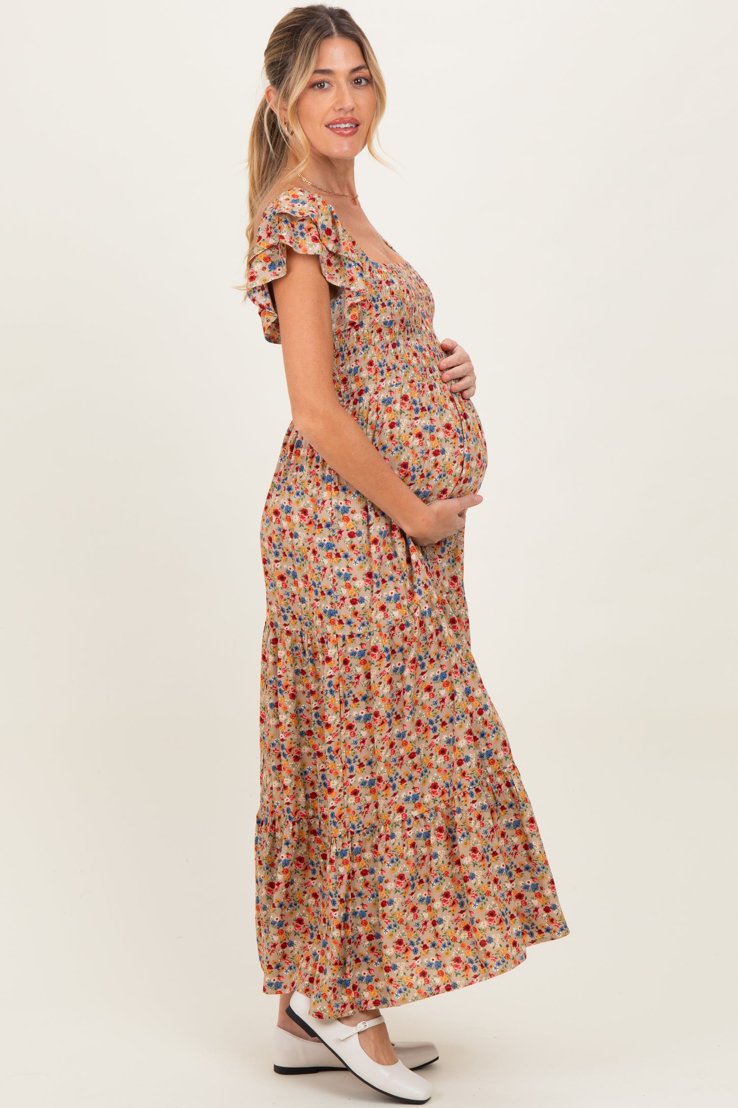 woman wearing a floral maternity maxi dress with ruffled sleeves and cradling her baby bump