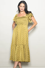 woman wearing a mustard yellow polka dot midi dress with smocked bodice and ruffled sleeves, posing with hands in pockets