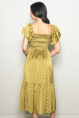woman wearing a yellow polka dot dress with short puff sleeves and a smocked back, standing against a neutral background