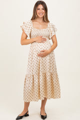 woman wearing a beige polka dot maternity dress with flutter sleeves and a fitted bodice, showing her baby bump