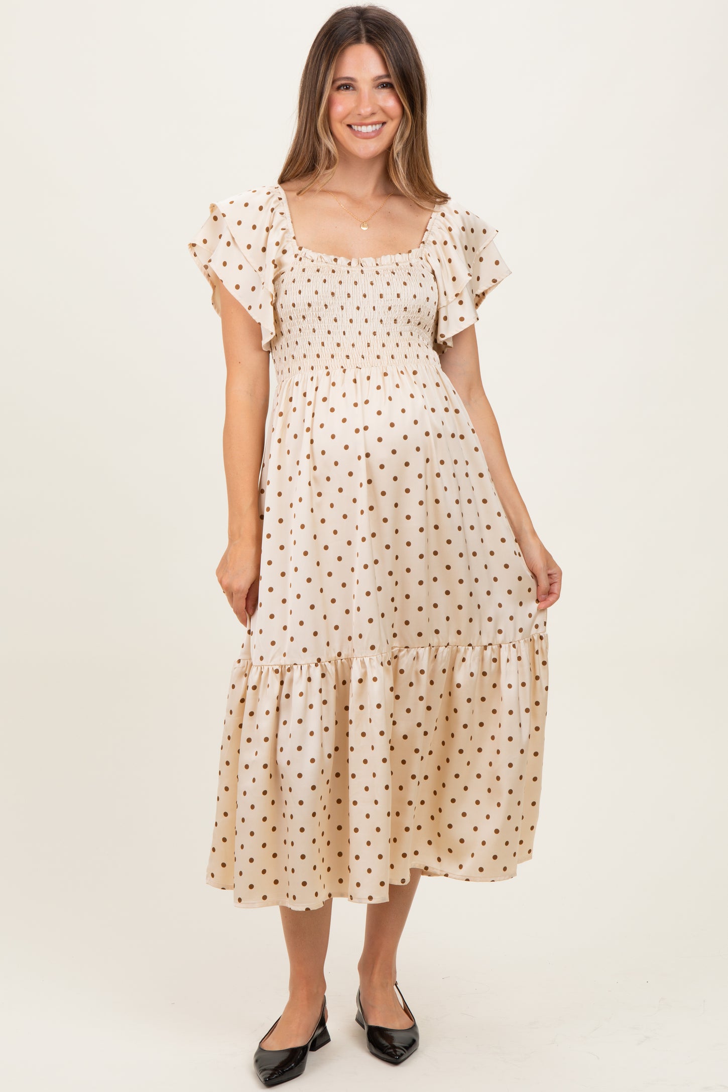woman wearing a cream maternity dress with brown polka dots and flutter sleeves, showing her baby bump