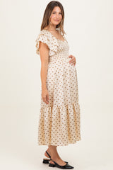 woman wearing a cream polka dot maternity dress with ruffled sleeves and a fitted bodice, holding her baby bump