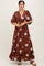 woman wearing a brown floral maxi dress with a v-neckline and puff sleeves, standing with hands on her hips