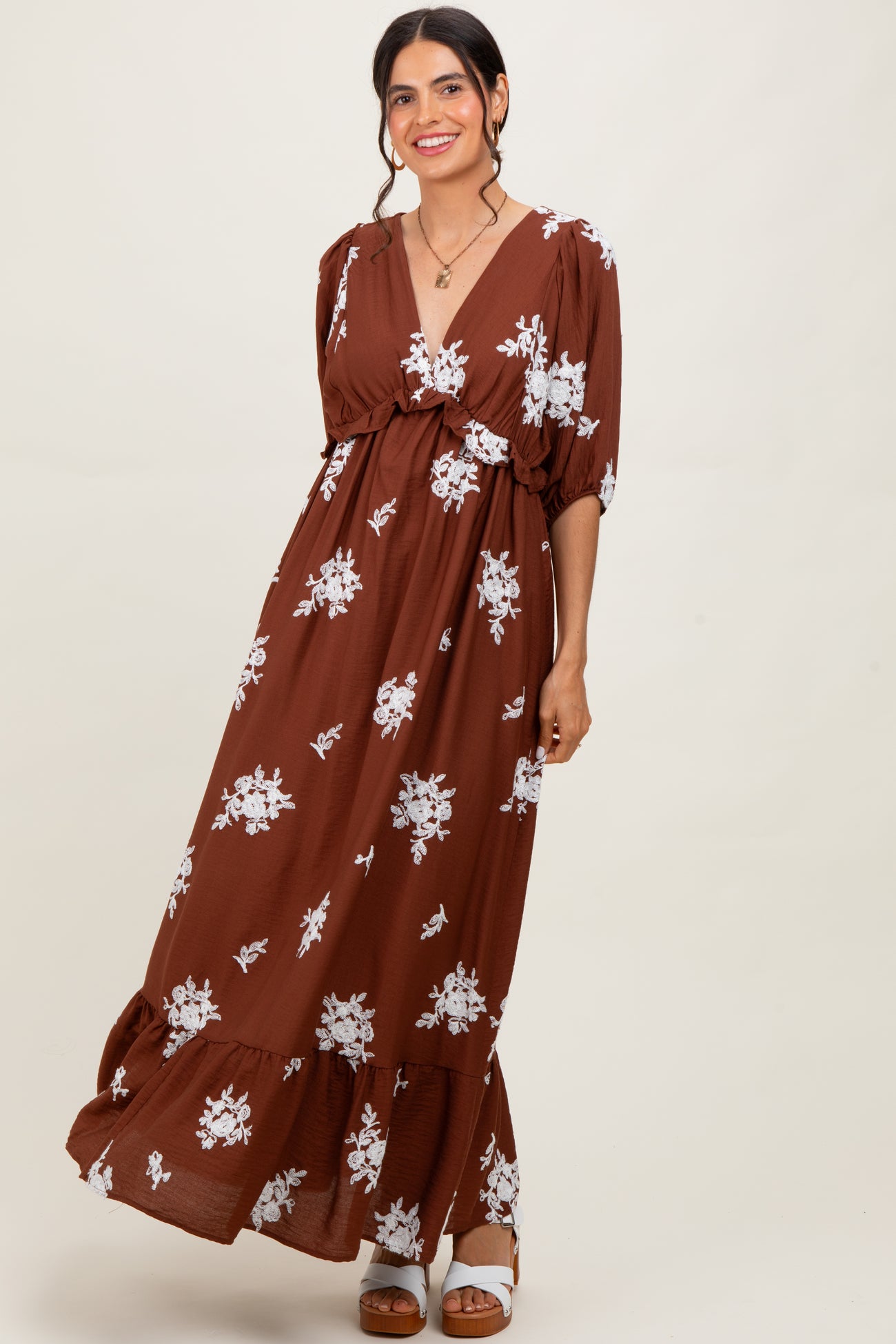 woman wearing a brown floral maxi dress with a v-neck and tiered skirt, posing with a smile