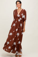 woman wearing a brown floral maxi dress with a v-neck and tiered skirt, posing with a smile