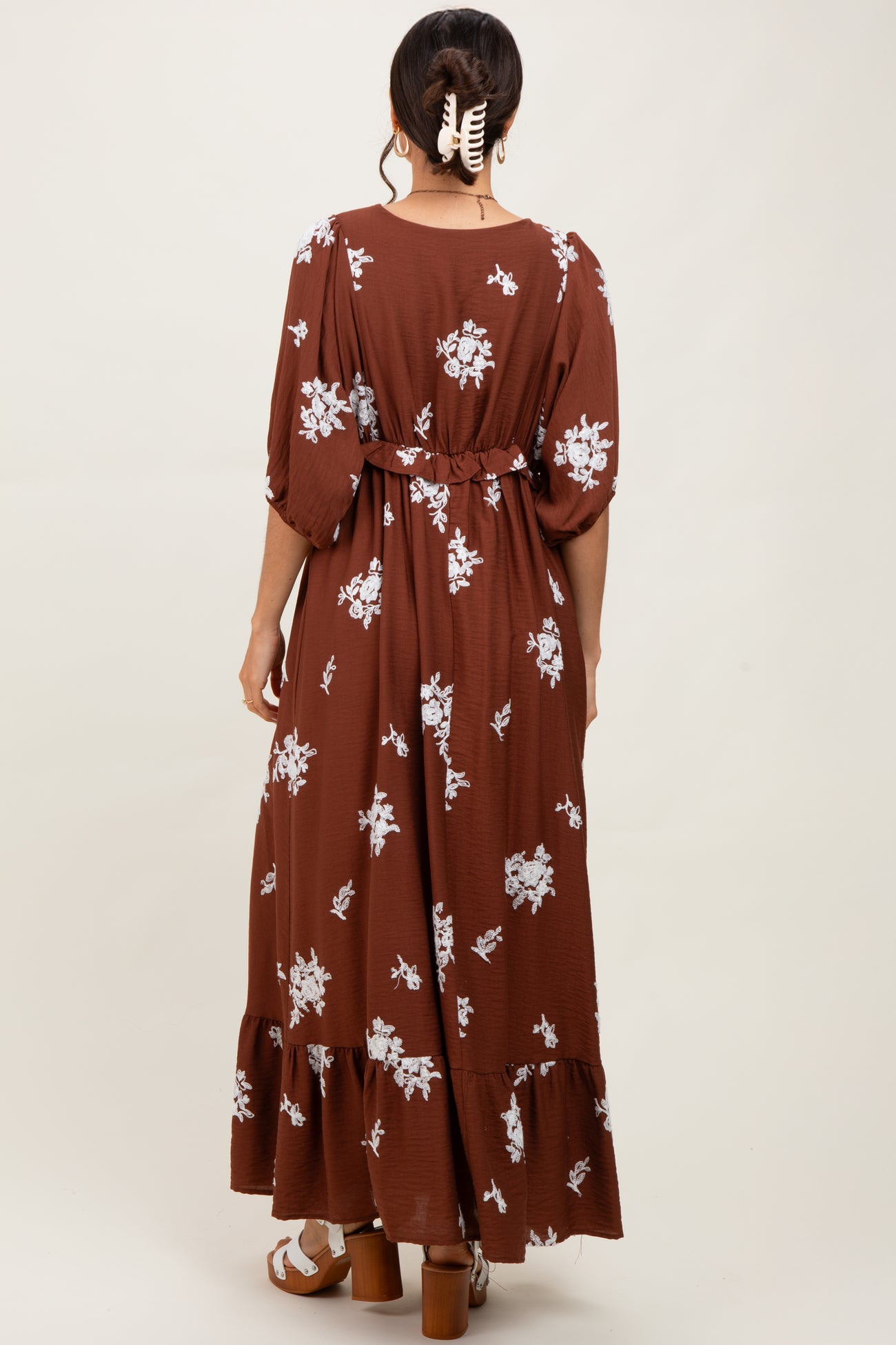 woman wearing a brown floral maxi dress with a cinched waist and tiered skirt, viewed from the back
