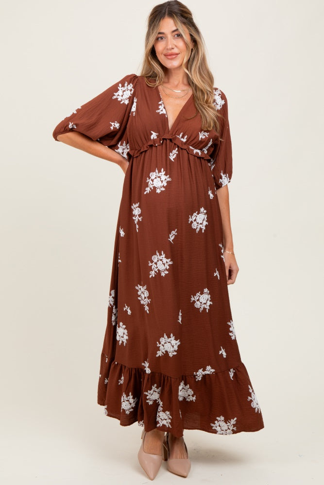 woman wearing a brown floral print maternity maxi dress with a tie waist and puff sleeves, showing her baby bump