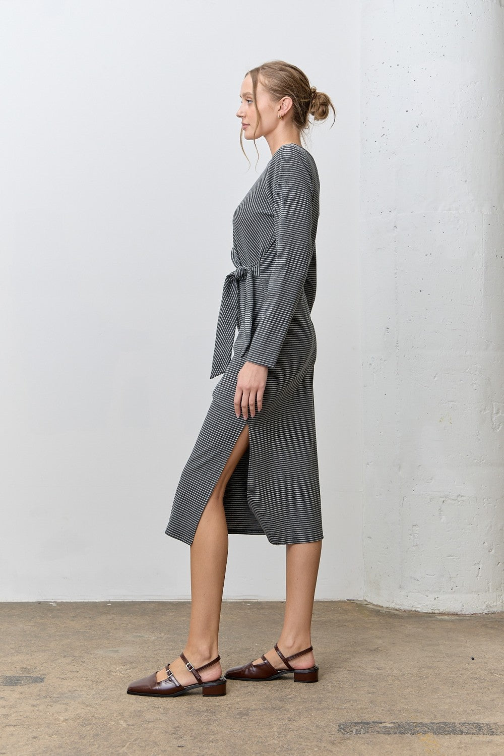 woman wearing a gray striped long sleeve midi dress with a side slit and a waist tie