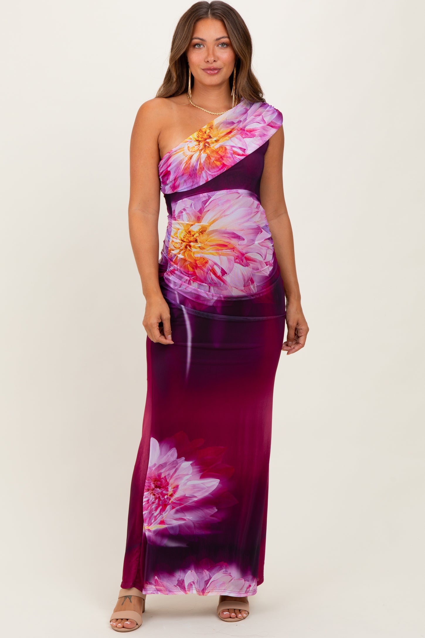 woman wearing a one-shoulder floral maternity dress in purple and pink tones with a fitted silhouette and maxi length