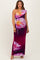 woman wearing a one-shoulder floral maternity dress in purple and pink tones with a fitted silhouette and maxi length