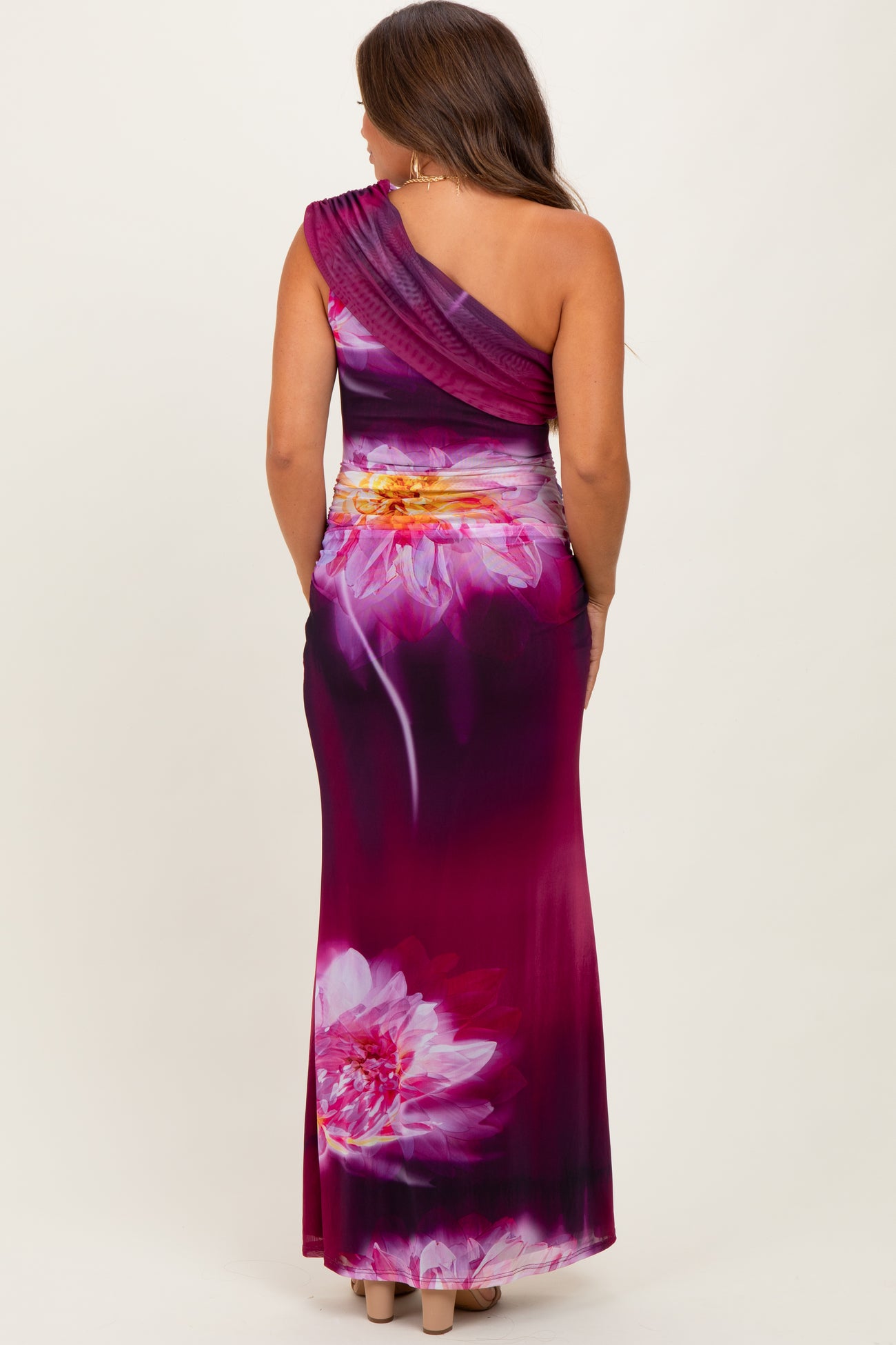 woman wearing a one-shoulder purple floral maternity gown with a fitted silhouette and a flowing skirt