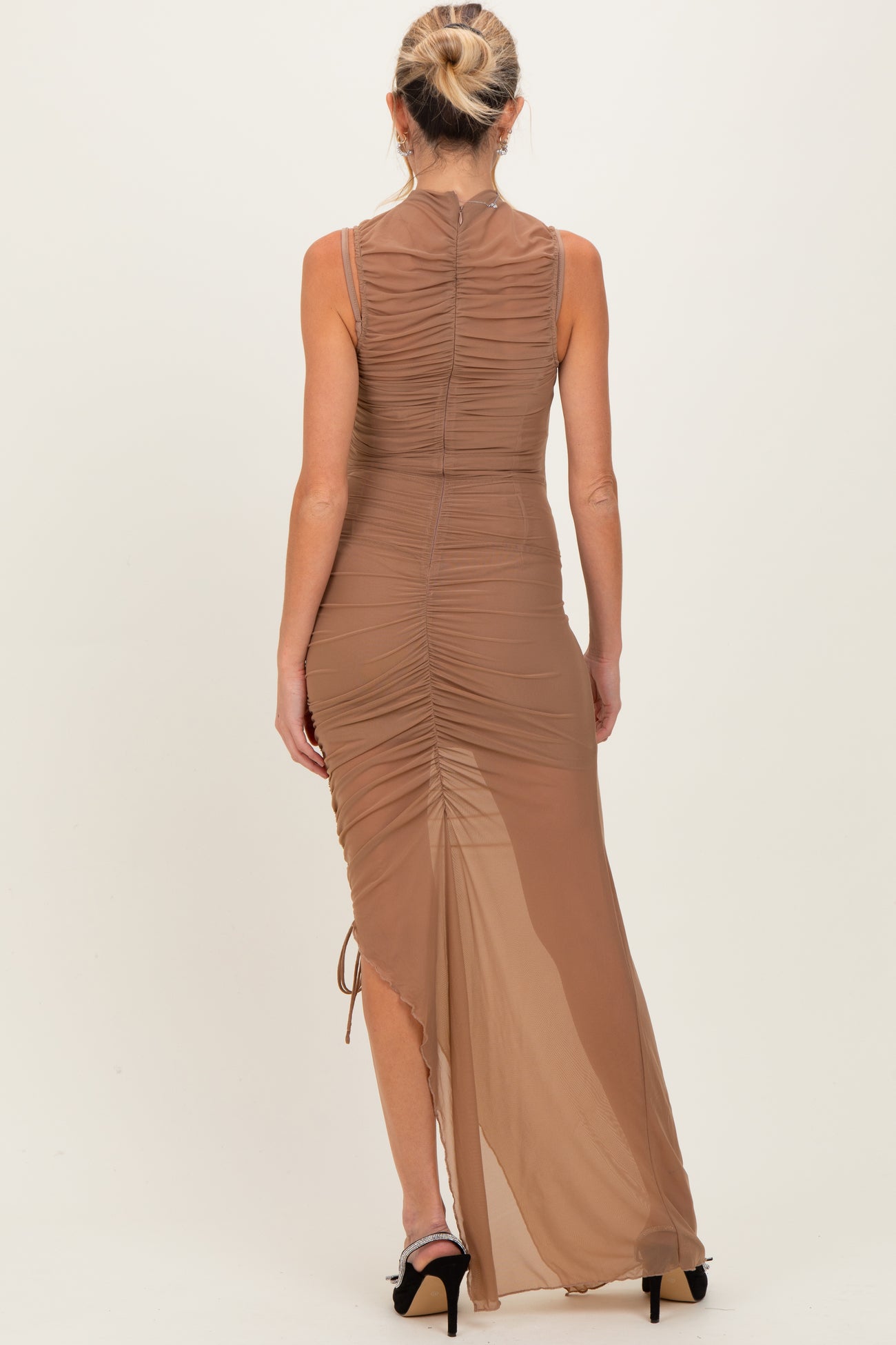 woman wearing a tan maternity maxi dress with ruching and a side slit, showing elegant back details